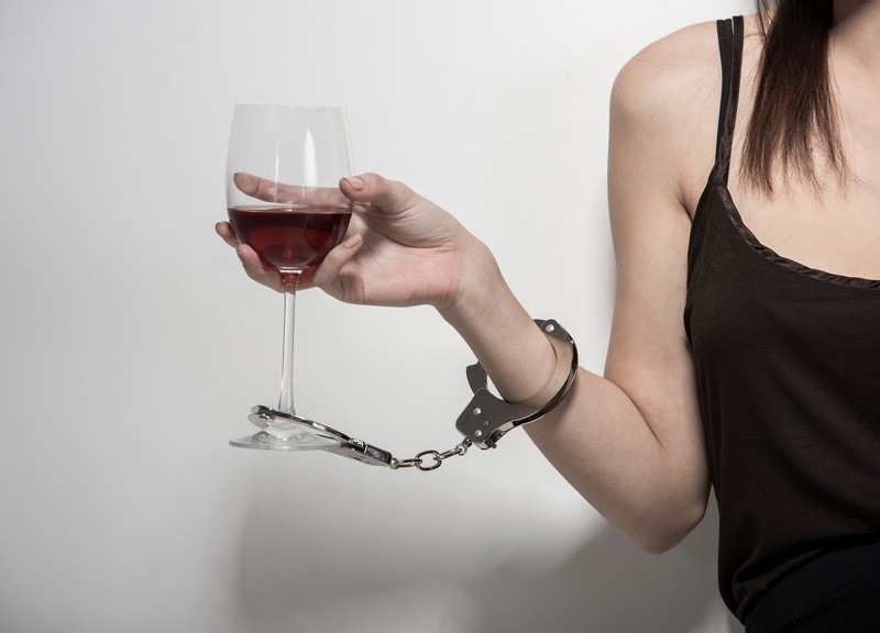 Young woman with a glass of wine and handcuffs. Addicted to drugs and alcohol.
